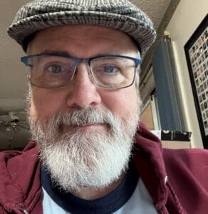 A man with white beard and glasses wearing a hat.