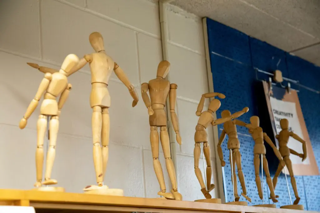 A group of wooden mannequins on display in front of a wall.